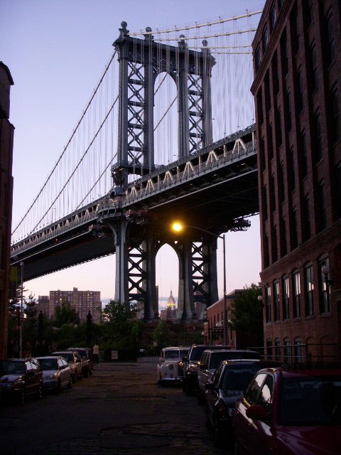 The Manhattan Bridge framed by red brick buildings along a Brooklyn street.